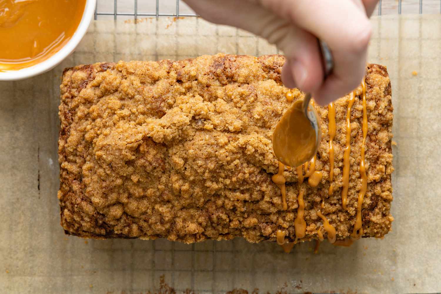 Dulce de Leche Drizzle Spooned in a Zig-Zag Motion Onto the Dulce de Leche Banana Bread Resting on a Piece of Parchment Paper on the Cooling Rack 