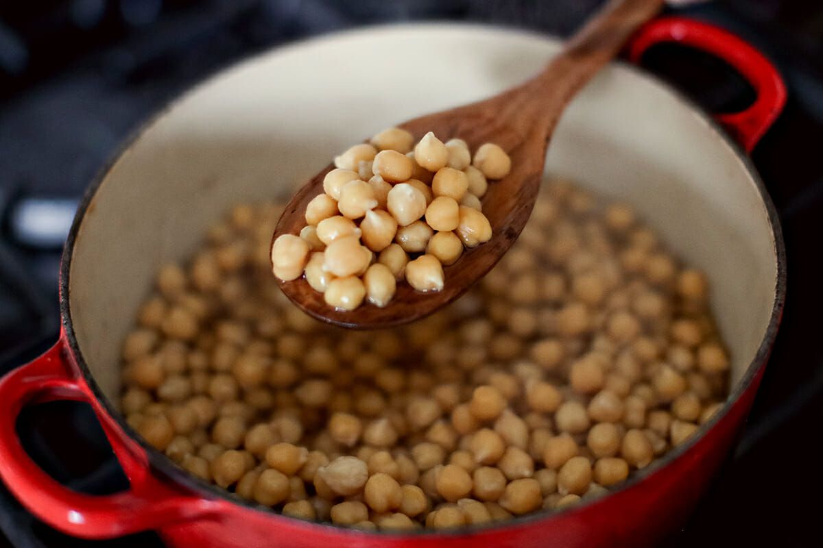A scoop of cooked chickpeas in a wooden spoon