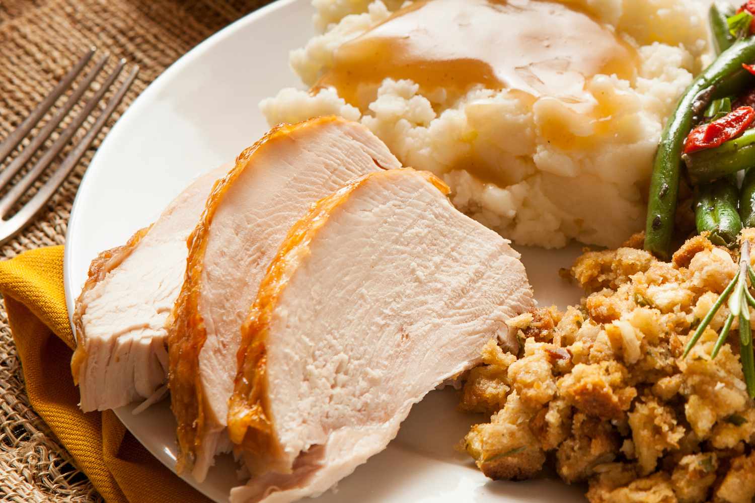 A plate of Thanksgiving food - sliced turkey, stuffing, mashed potatoes and green beans