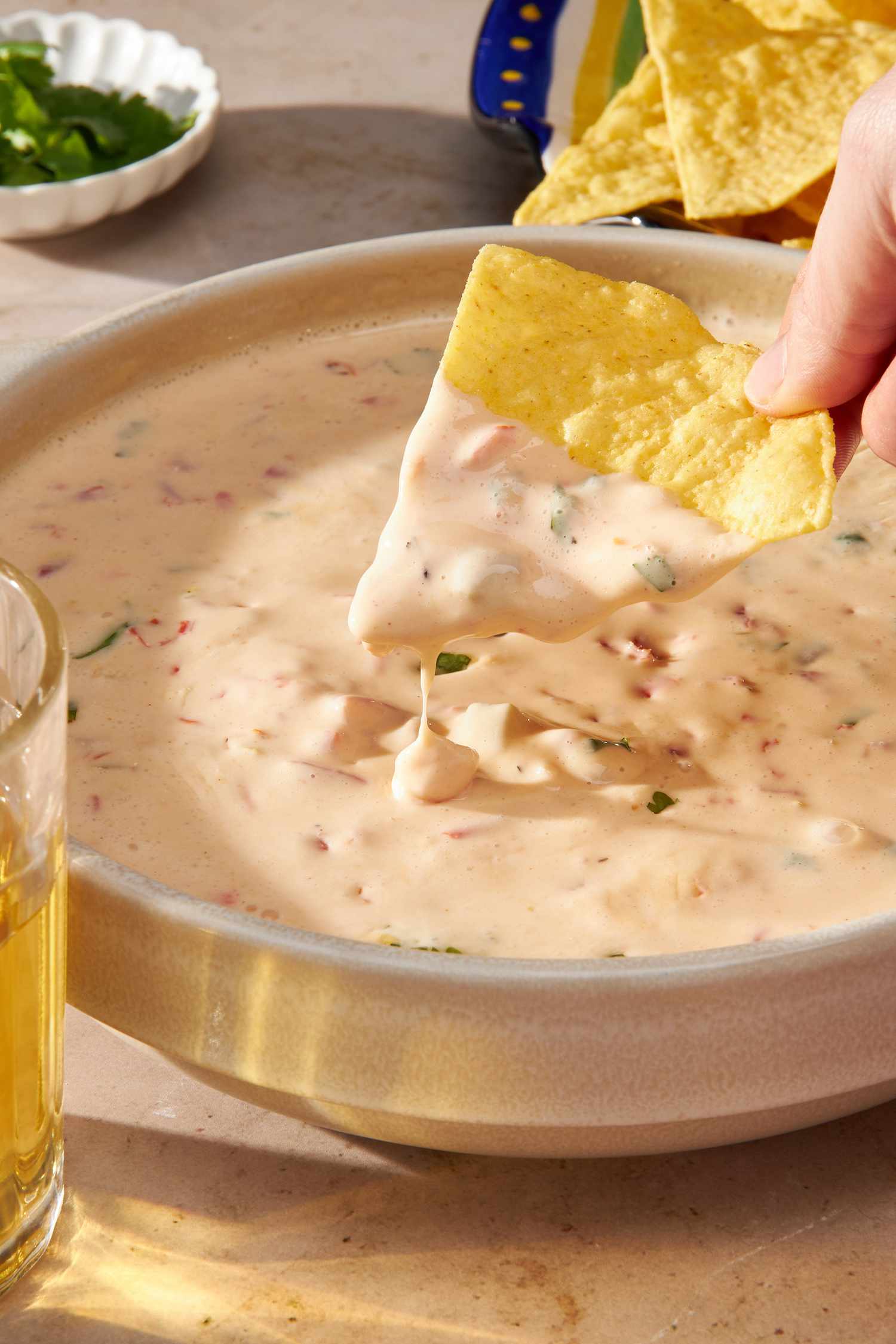 Corn chip with chile con queso cascading off it into a bowl with more chile con queso (at a table setting)