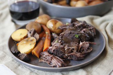 Perfectly tender crock pot roast piled onto a gray plate with carrots and potatoes and covered in gravy.
