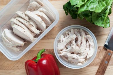 Plastic containers of poached chicken on a cutting board