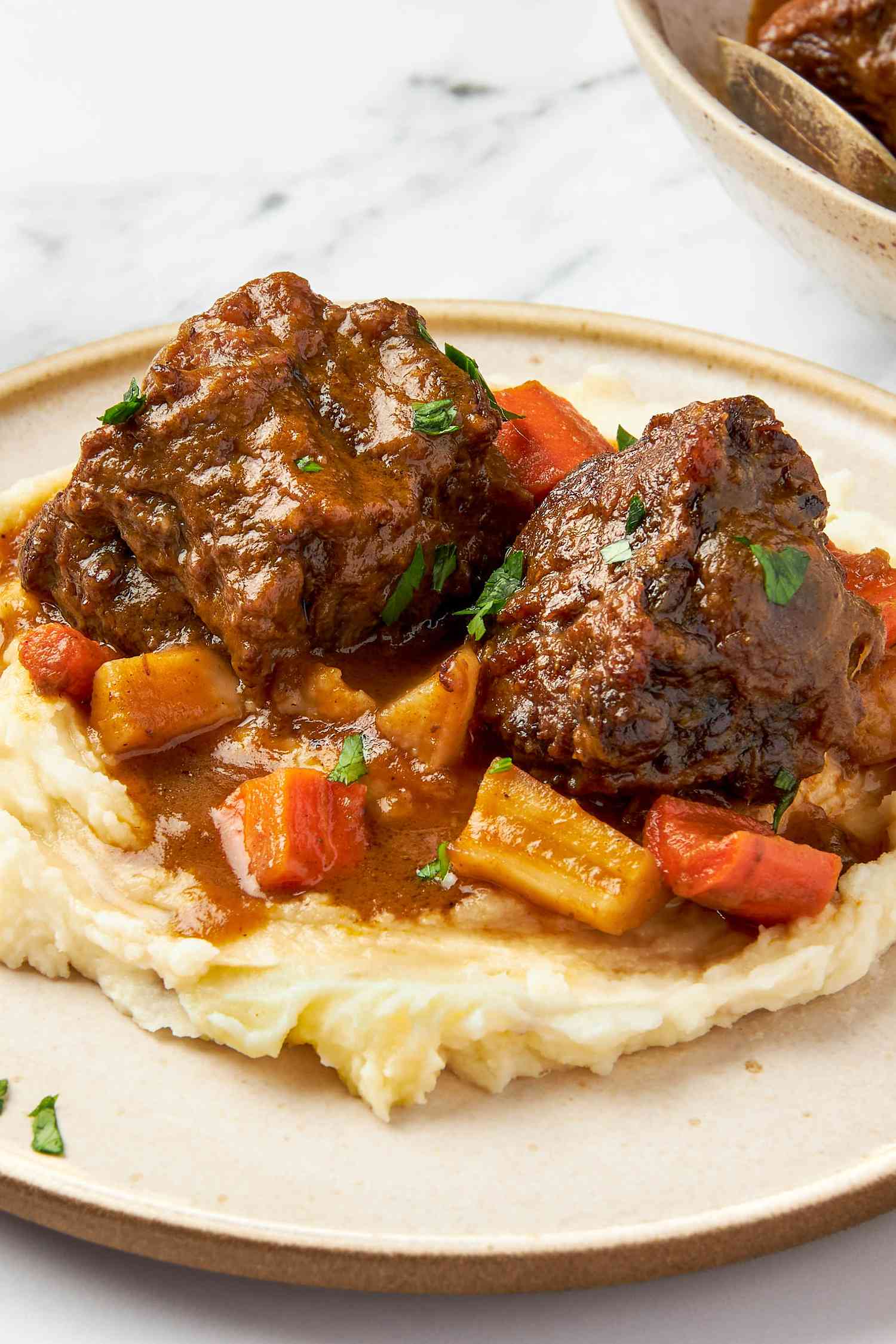 A plate with two braised oxtails and sauce over mashed potatoes
