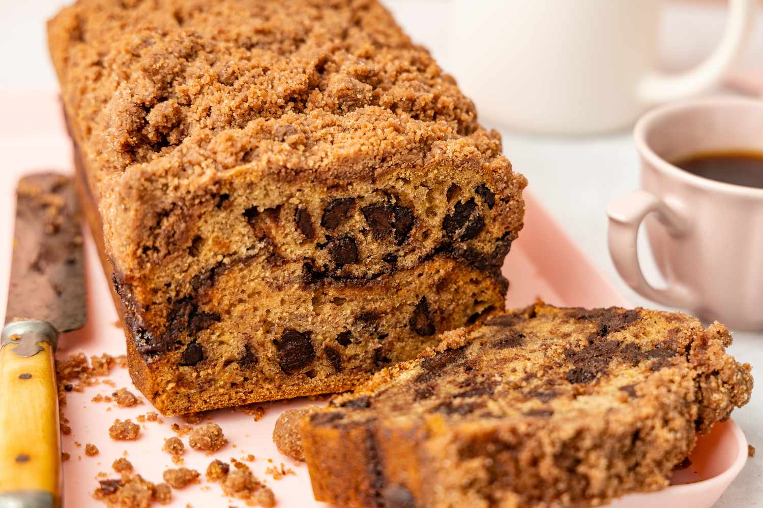 Loaf of Chocolate Chip Banana Bread Cake on a Platte, and in the Surroundings, a Knife and a Cup of Coffee