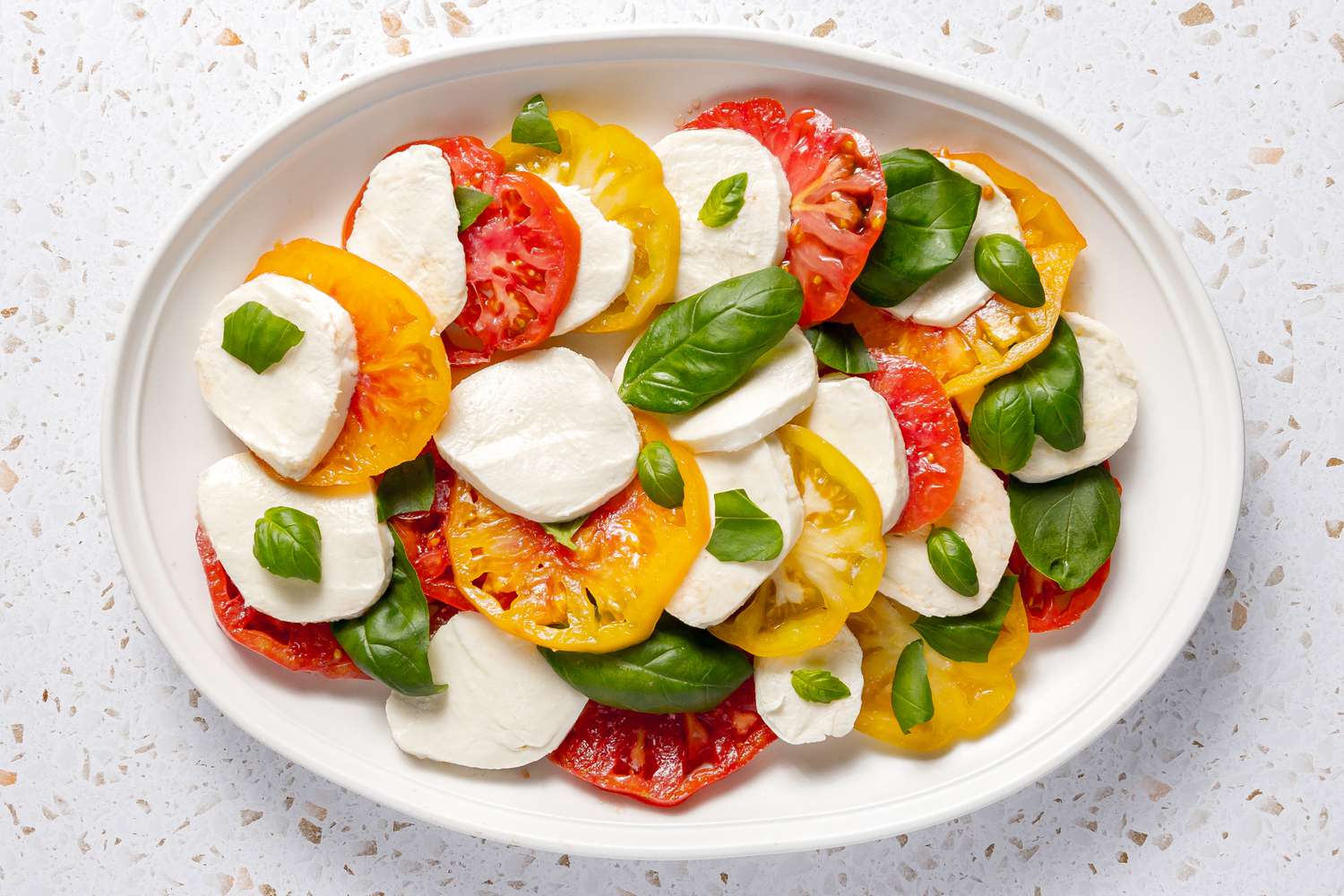 Heirloom Tomato Slices Plated With Sliced Mozzarella and Topped With Basil Leaves (Some Whole, Some Broken into Pieces)