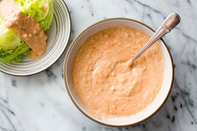 A bowl of Thousand Island Dressing with a spoon in it; a dressed wedge salad is to the side