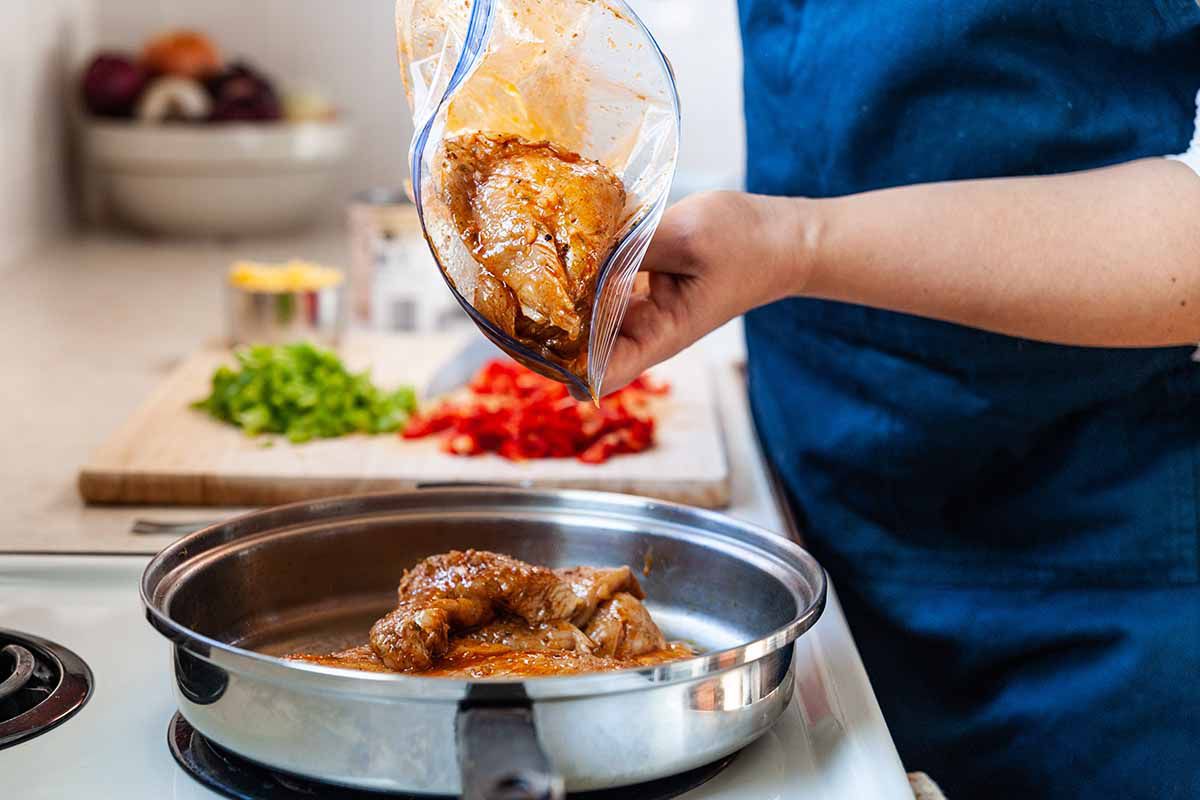 Easy Chicken Freezer Meal with Boneless Skinless Chicken Breast - woman pouring marinated chicken breasts out of ziploc bag into skillet