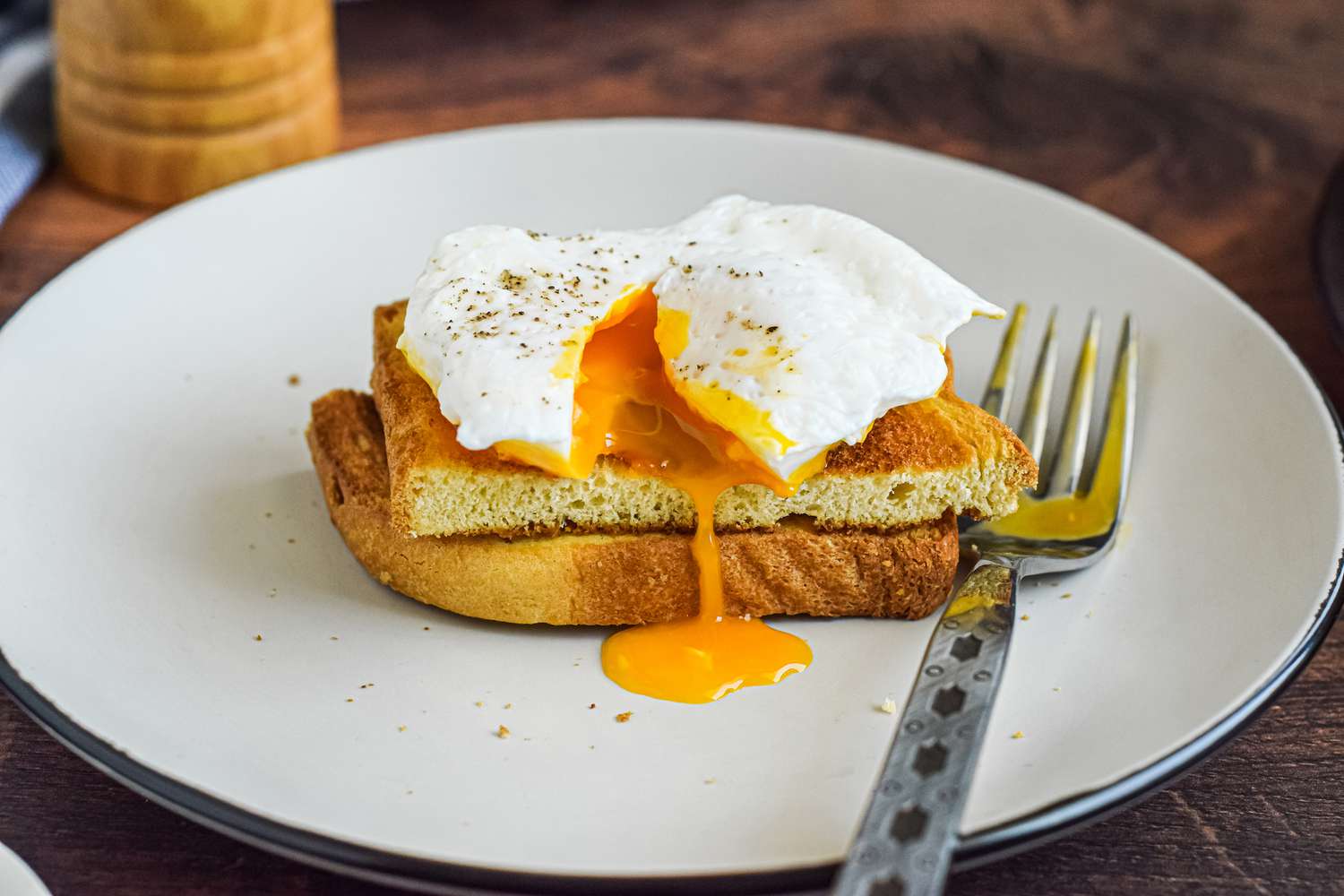 A poached egg on halved toast with the yolk running over the side.