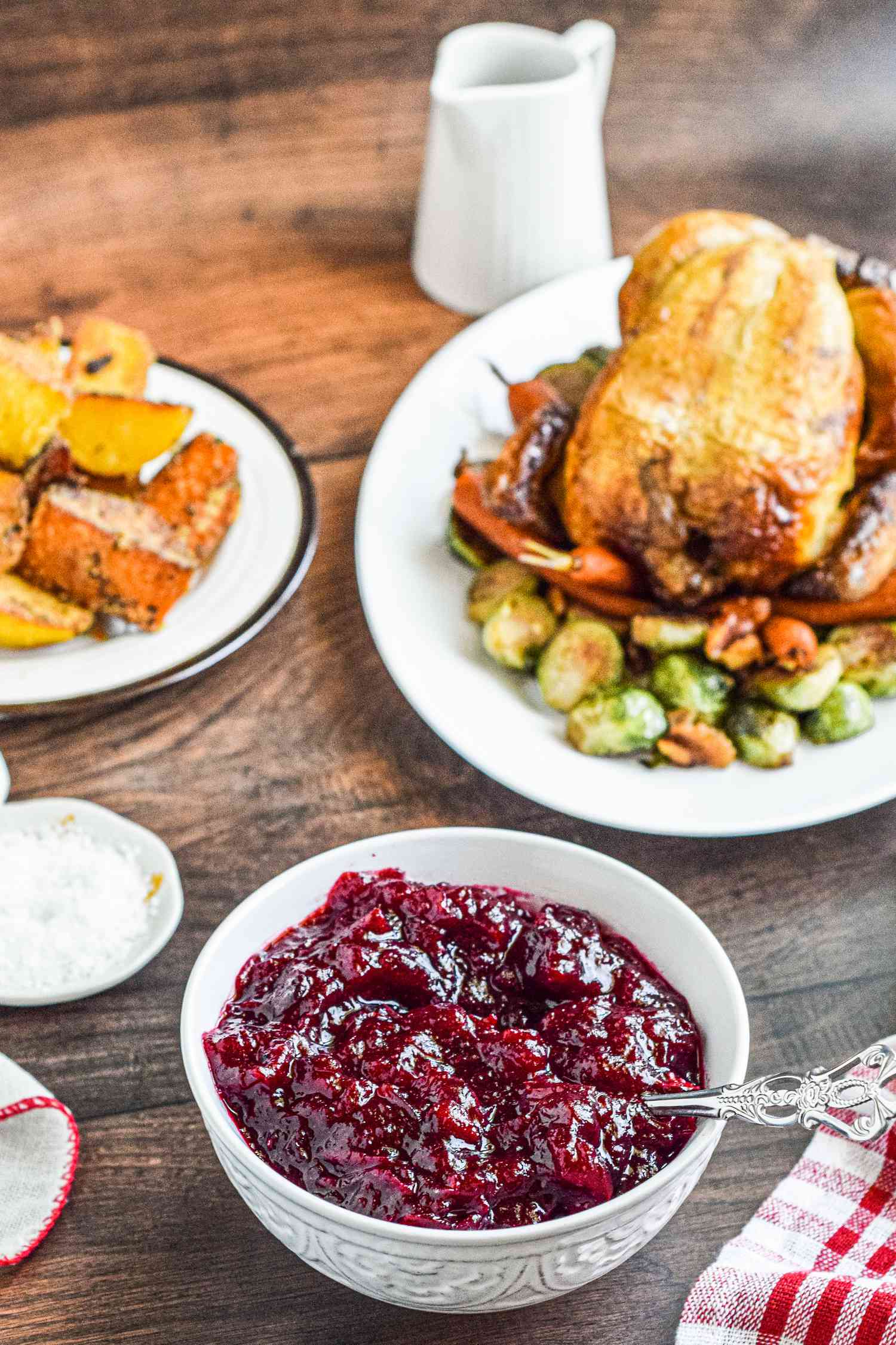 A Thanksgiving table set with a bowl of cranberry sauce next to a platter of turkey and other sides.