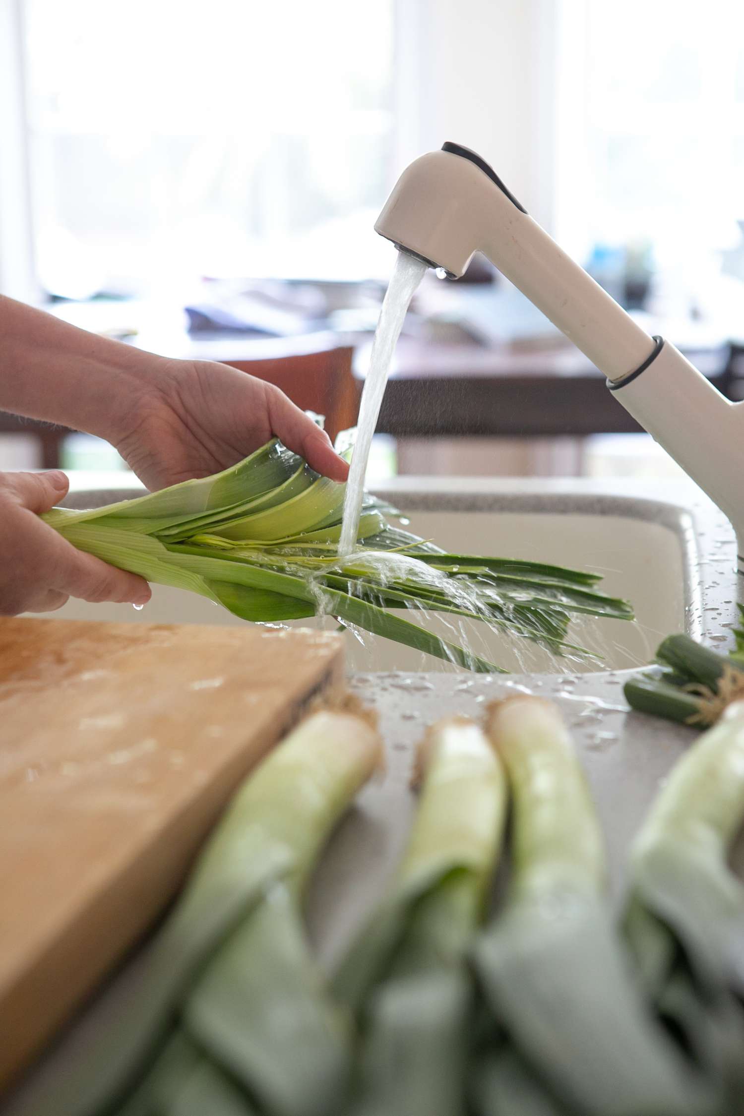 Leeks Washed at a Kitchen Sink in the Background, and in the Foreground, a Cutting Board and Four Washed Leeks on the Counter