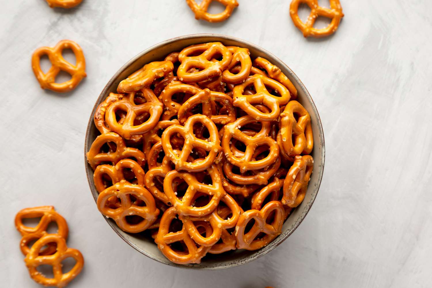 Overhead view of a brown bowl of crunchy mini pretzels on a gray background