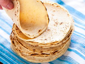 Corn tortilla recipe with corn tortillas stacked on a blue striped linen.