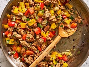 A skillet of cooked ground turkey and bell peppers with a wooden spoon in it
