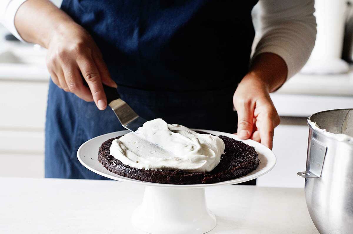 Authentic Black Forest Cake with the first chocolate layer getting whipped cream spread on top.