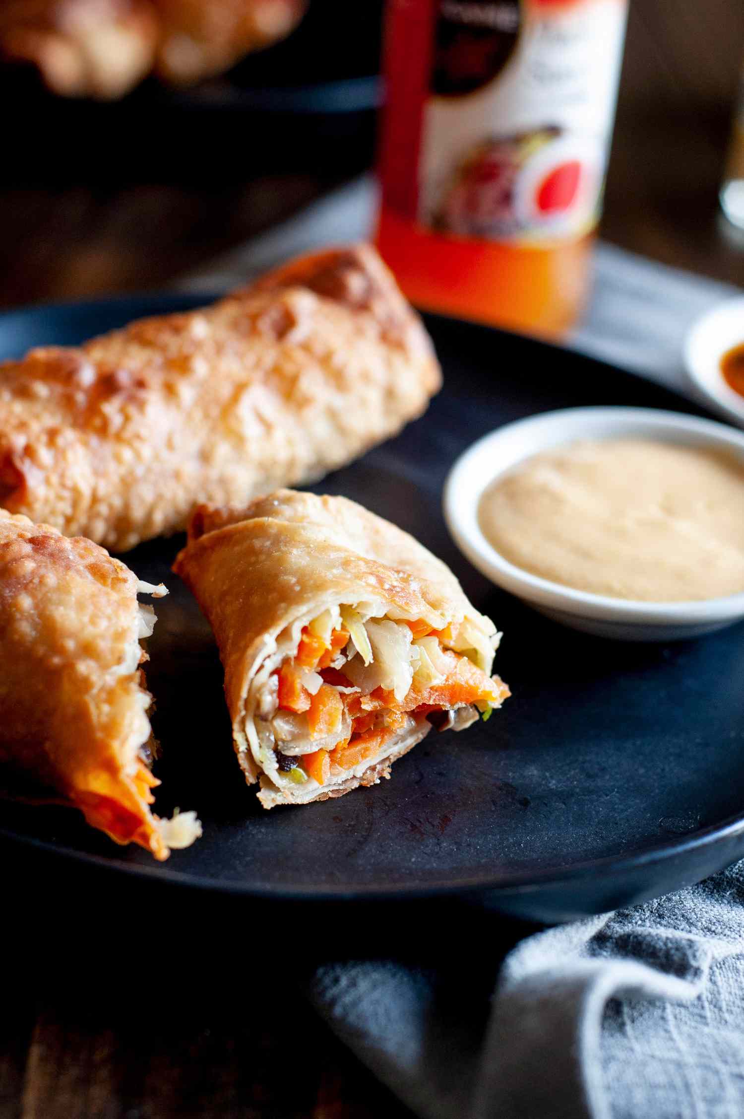 A dark plate with stacked vegetable egg rolls and dipping sauce