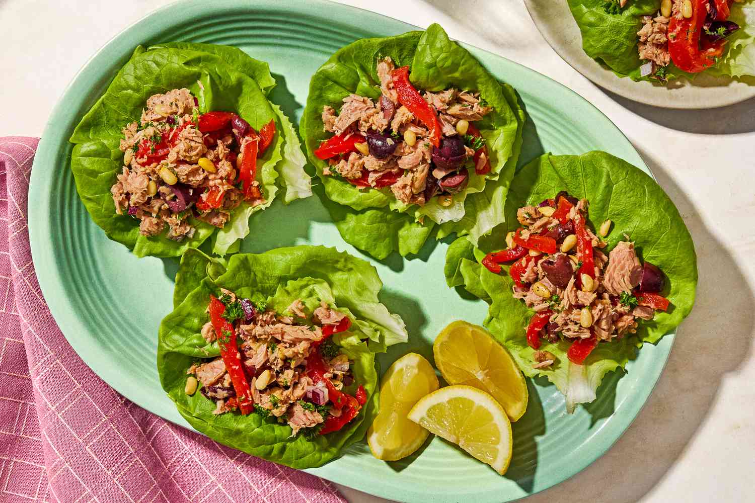 Overhead view of a plate of italian-style tuna salad on four lettuce leaves next to lemon slices