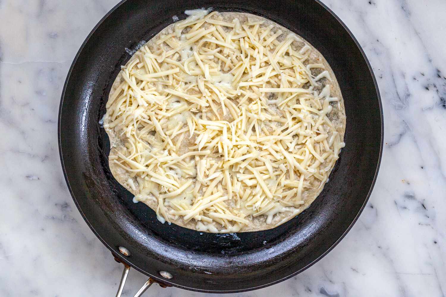 A tortilla topped with cheese in a skillet for a quesadilla recipe.