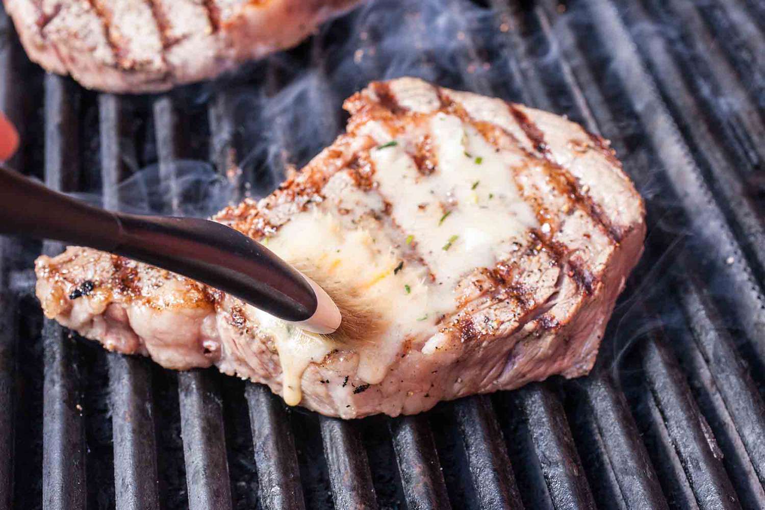 Steak on the rill being basted with butter