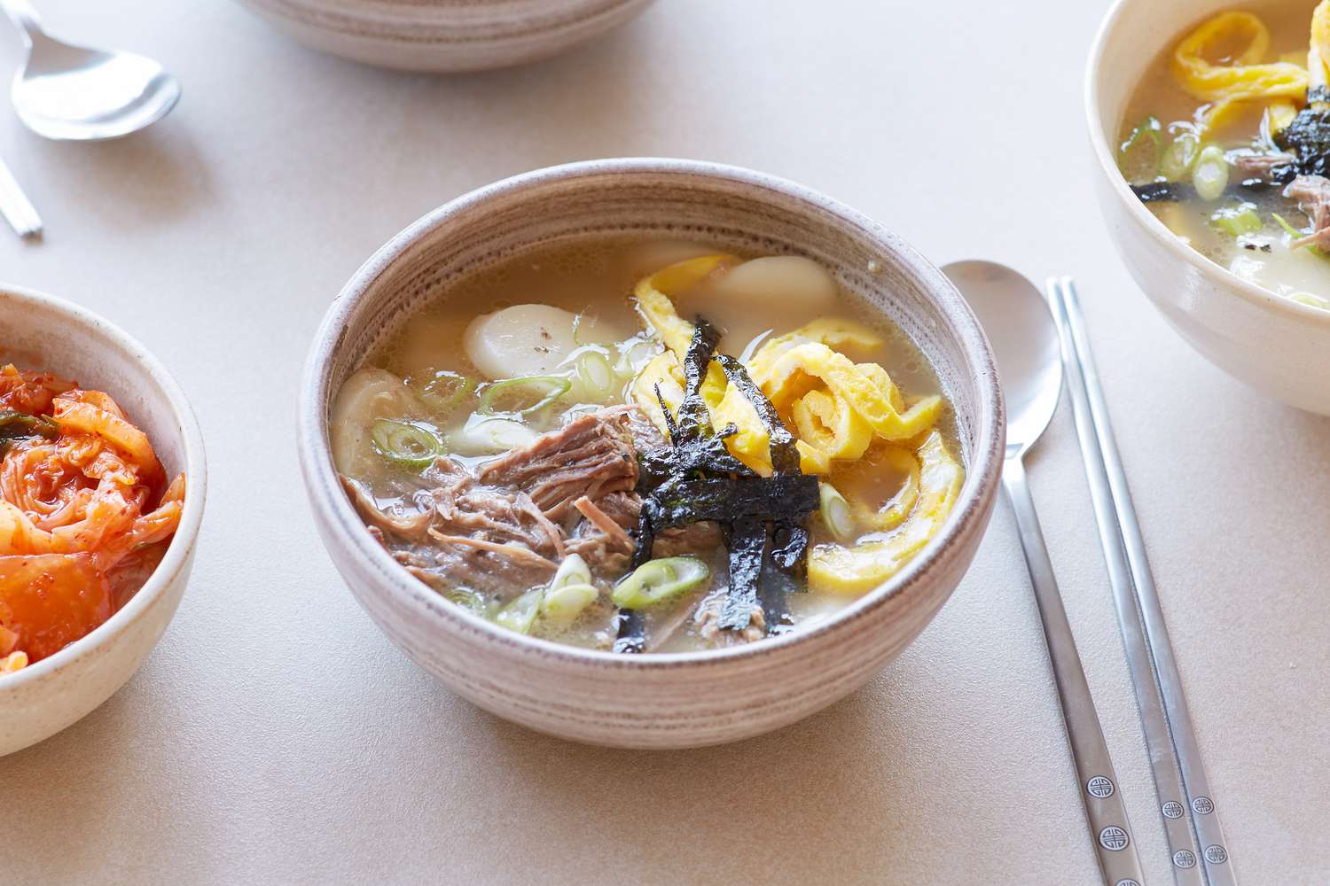 A table set with a bowl of Dduk guk (Korean rice cake soup) and spoons.