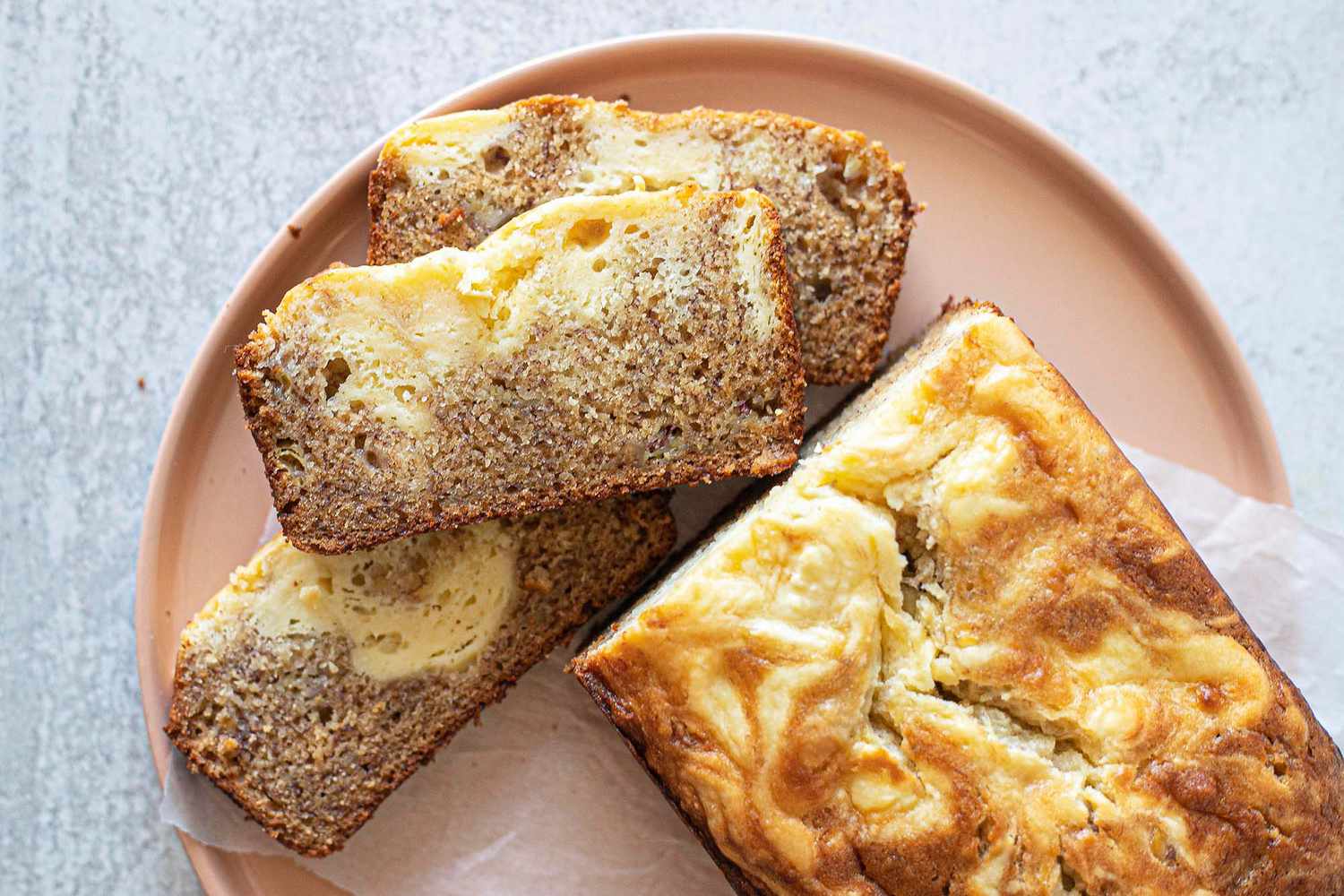 Overhead view of a loaf of banana bread with cream cheese on a plate. Three slices are laying in front of the loaf.