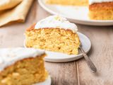 single slice of clementine cake on a small plate with a fork and the rest of the cake in the background