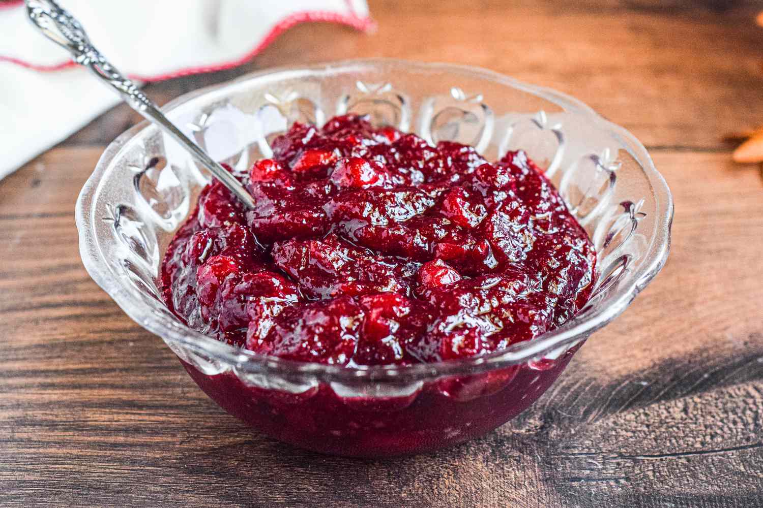 A glass bowl of cranberry sauce on a table with a spoon.