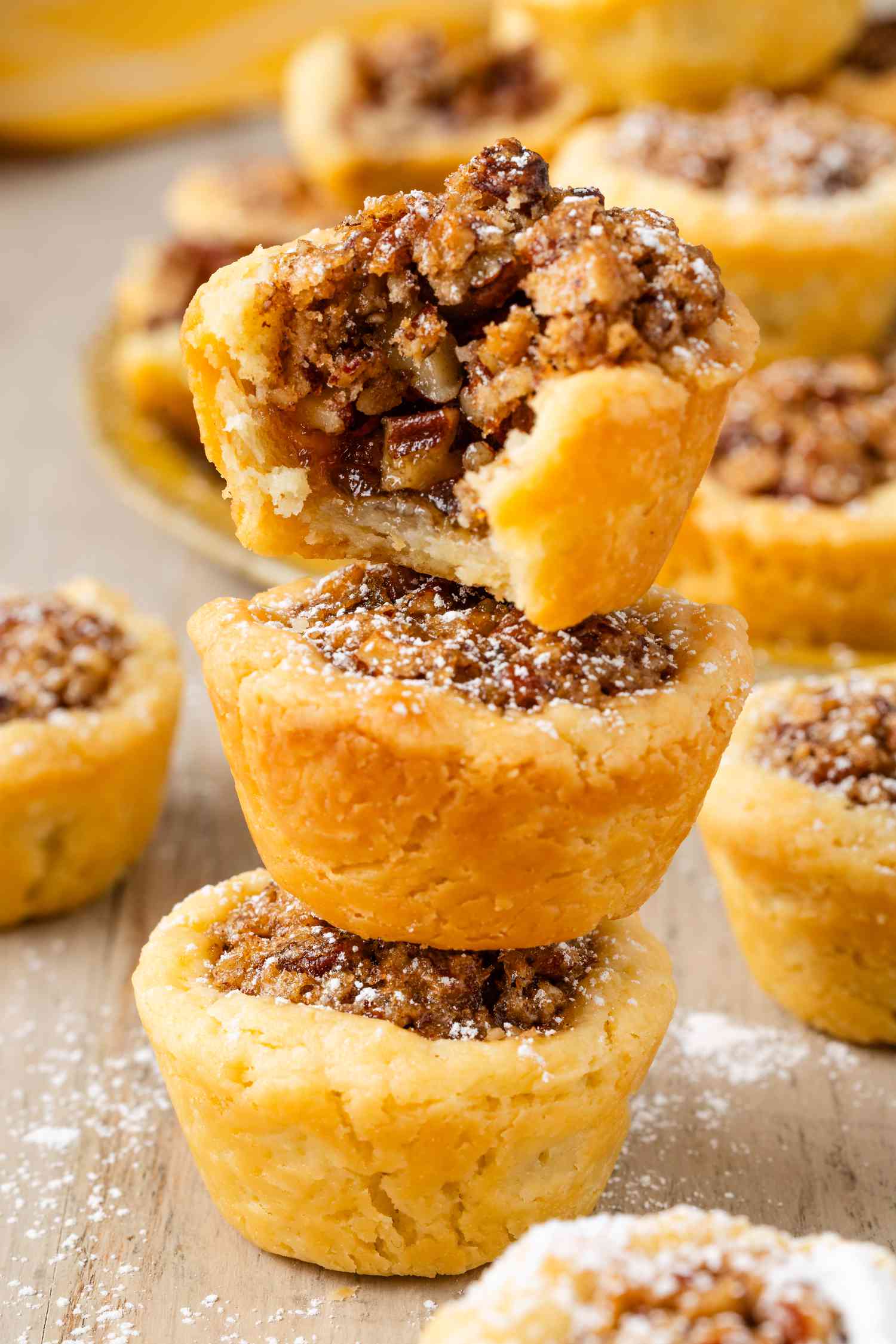 Stack of three pecan pie cookies on a counter (top cookie bitten into), and in the surroundings, more pecan pie cookies on the counter and on a plate