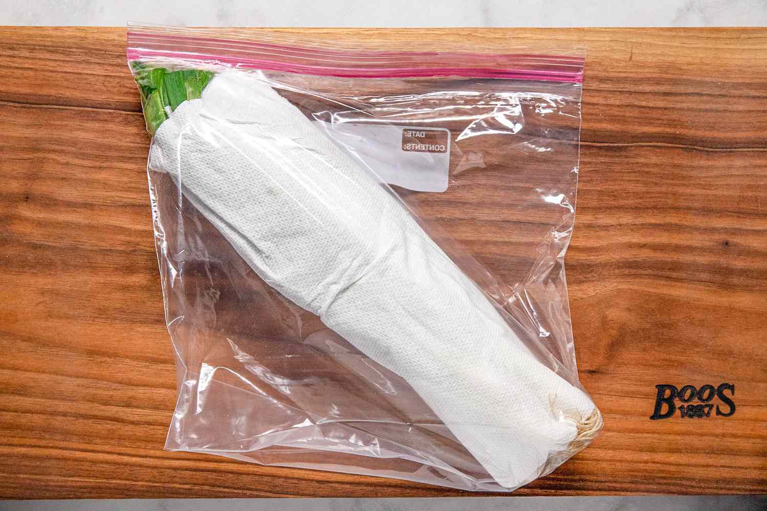 Green onions rolled up between paper towels stored in a zip-top plastic bag