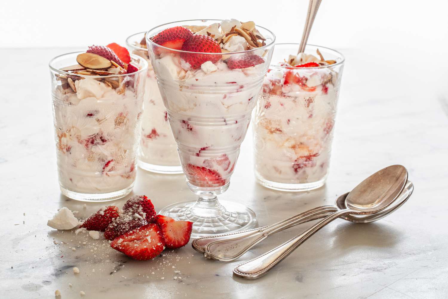 Glasses and Parfait Cups of Strawberry Eton Mess with Some Strawberries and Spoons on the Counter