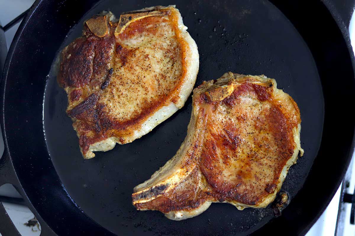 Two bone-in pork chops cooked on the stovetop.