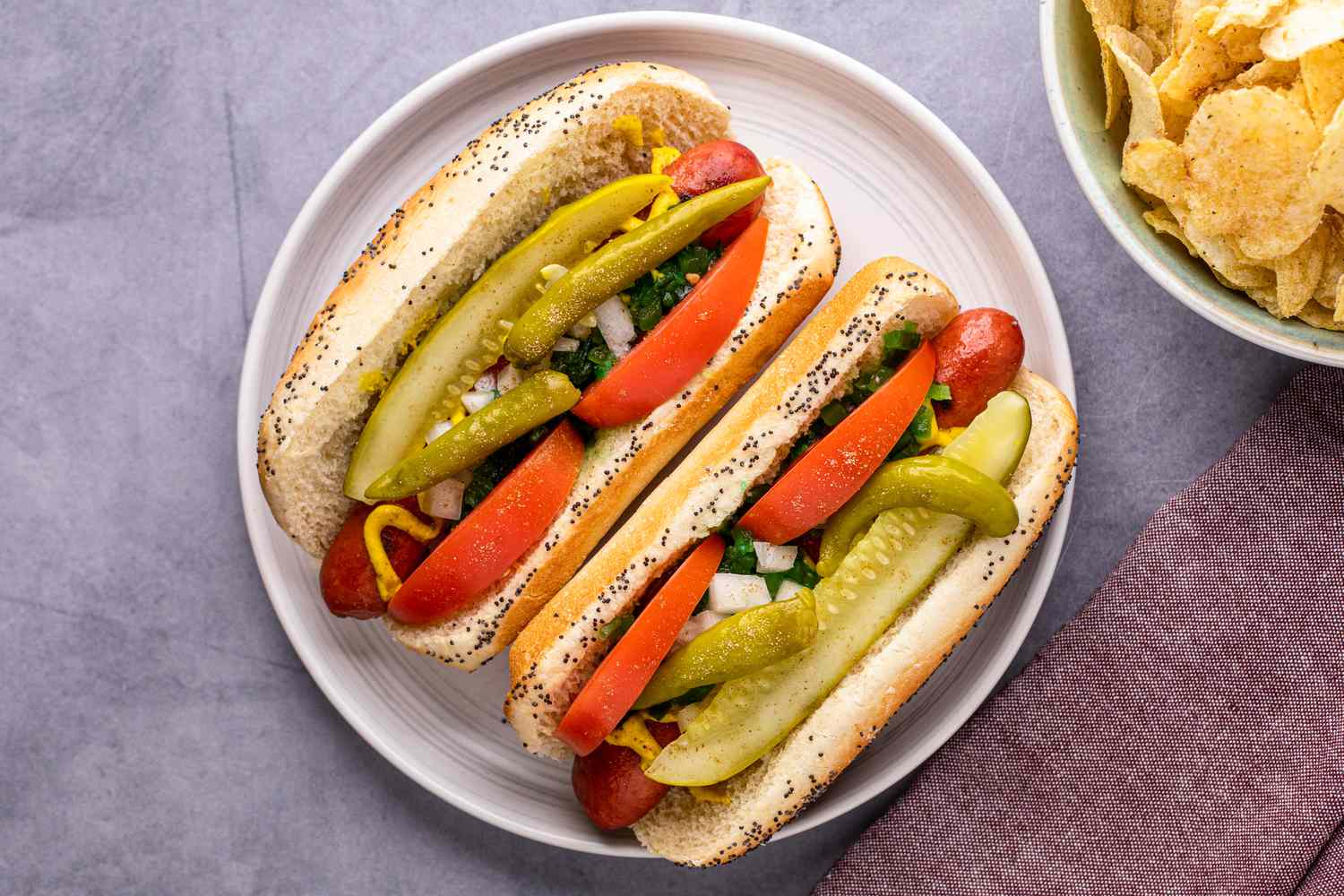 Overhead view of two Chicago dogs on a plate and topped with tomatoes and pickles.