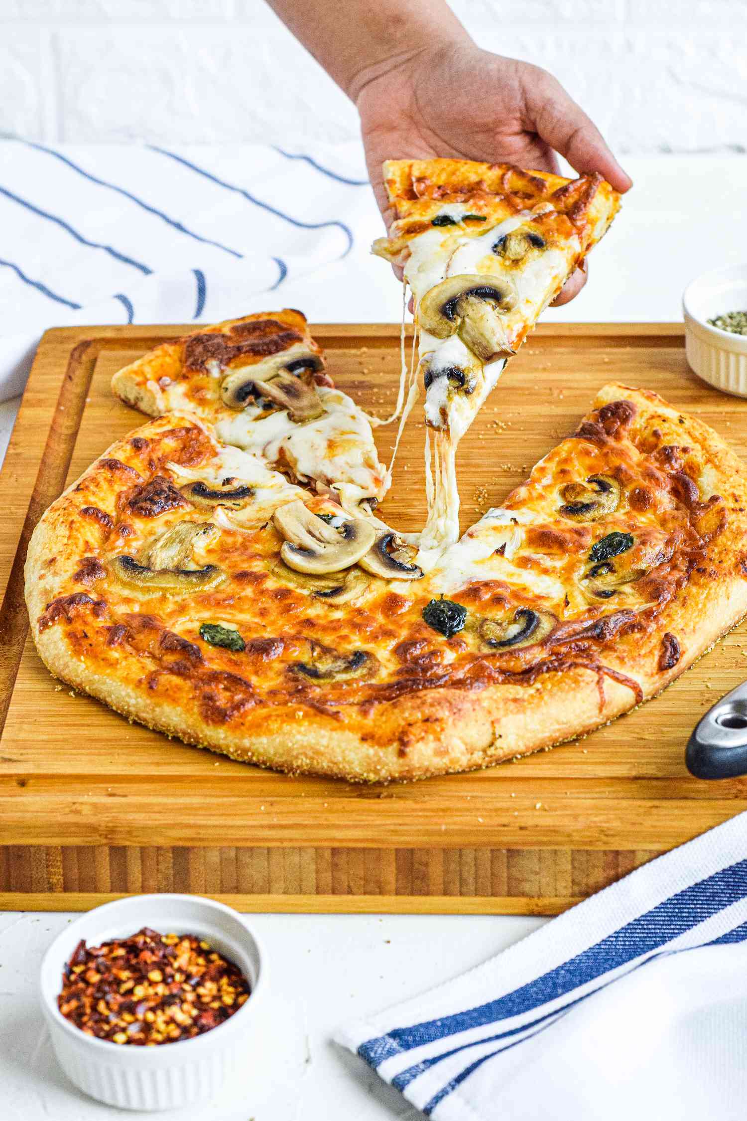 Side view of a cheesy homemade pizza recipe on a wooden cutting board.