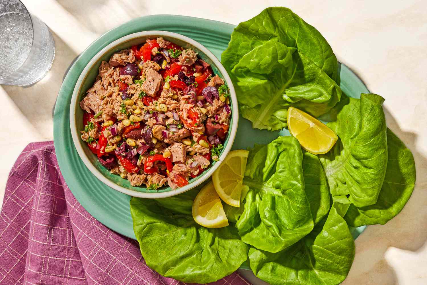 Overhead view of a bowl of italian-style tuna salad on a plate with lemon slices and lettuce