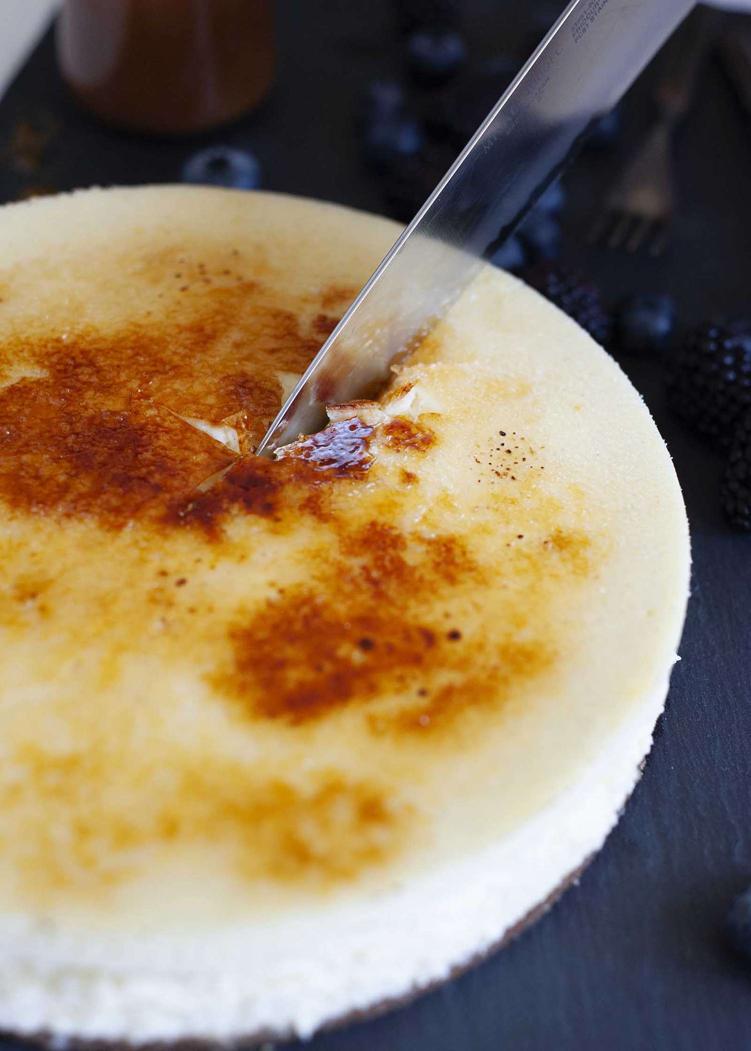 A knife slicing through the brittle topping of the best creme bruelee cheesecake