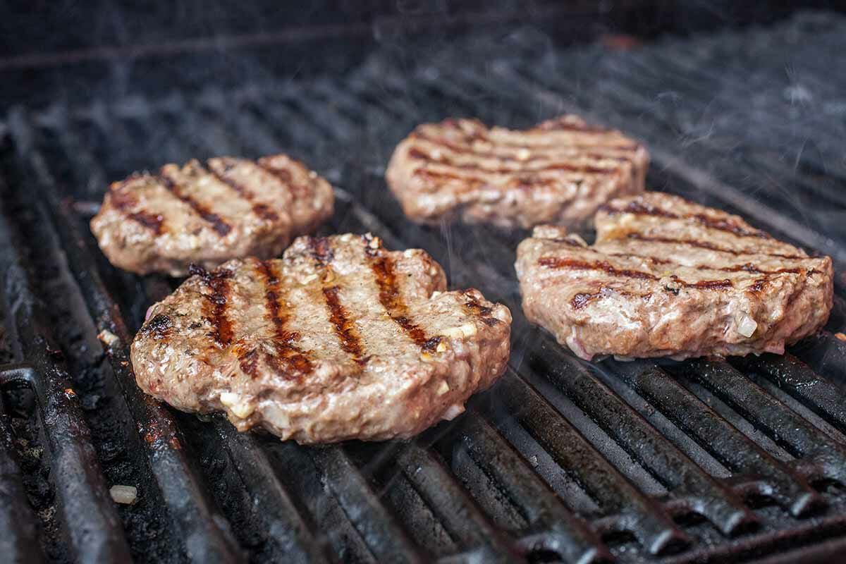 Four burger patties cooking on a grill