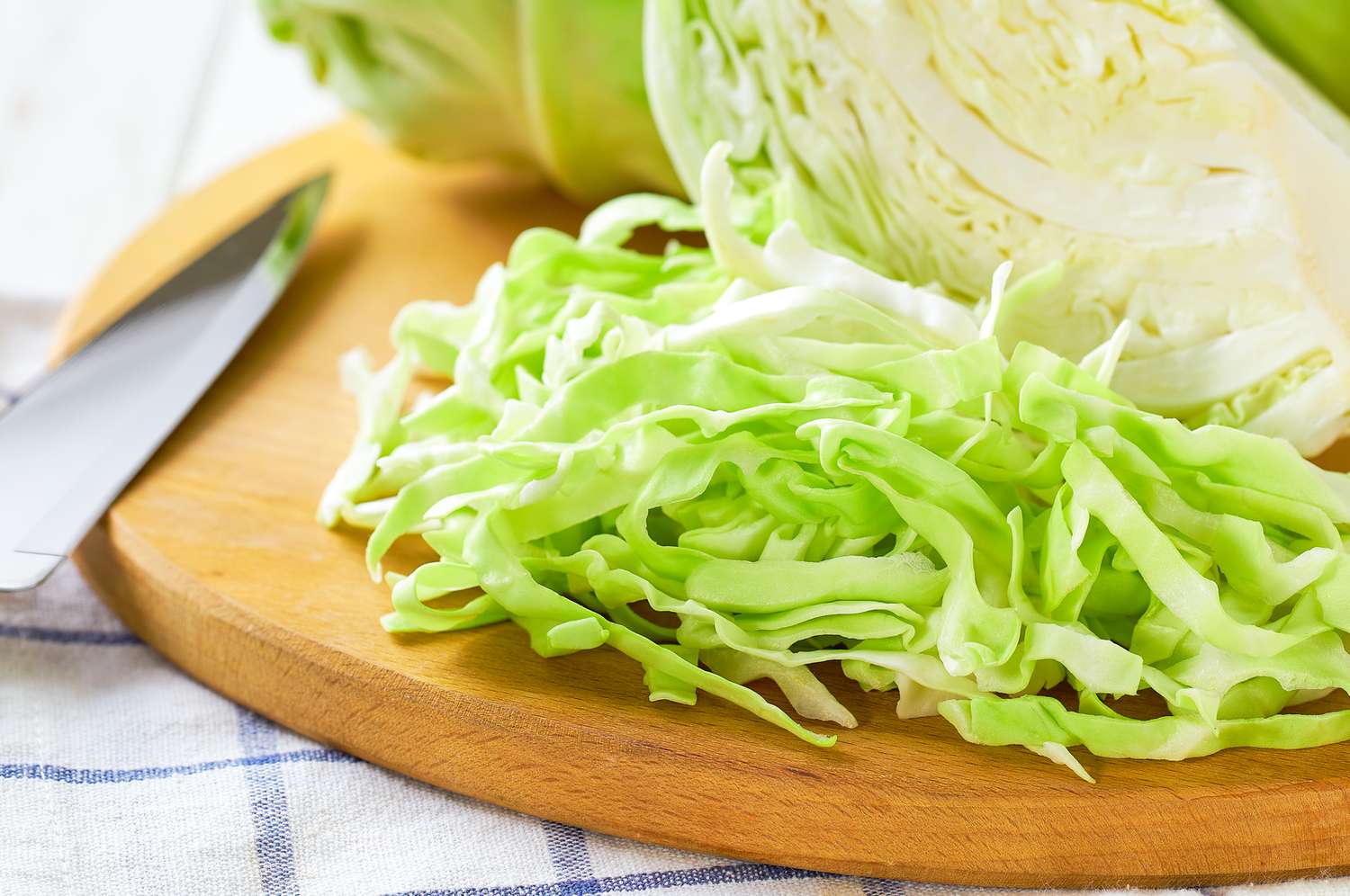 Shredded cabbage on a wooden cutting board next to a chef knife