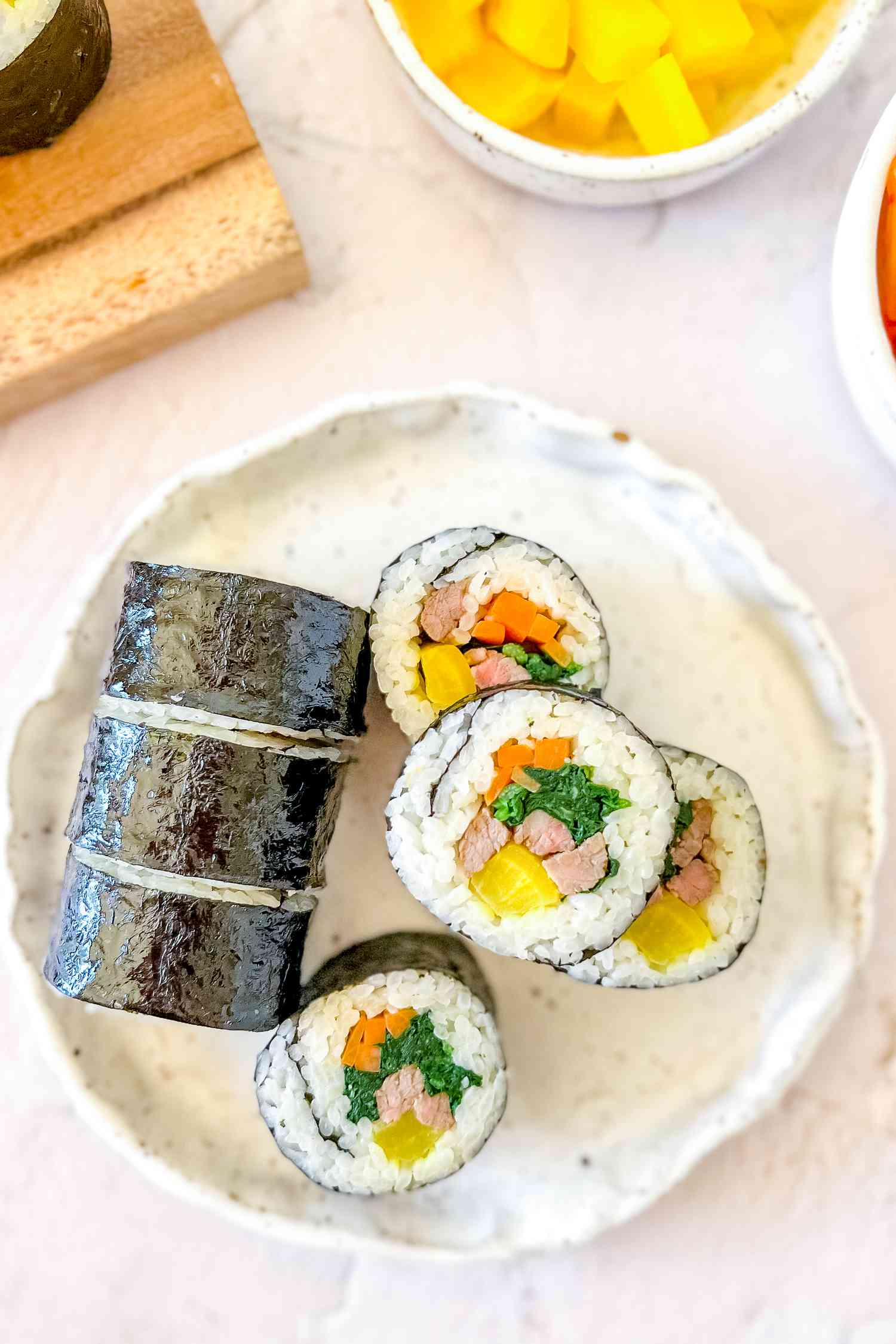 Korean Seaweed Rice Roll on a Plate Next to Wooden Plaque and a Small Bowl of 