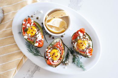 Overhead view of a platter of baked eggs in avocado and lemon slices.