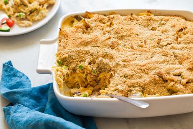 Angle view of a white baking dish of chicken tetrazzini with a slice removed next to a blue cloth napkin