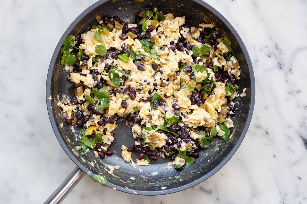 Overhead view of a skillet with scrambled eggs, black beans and cilantro mixed together for simple breakfast quesadillas.