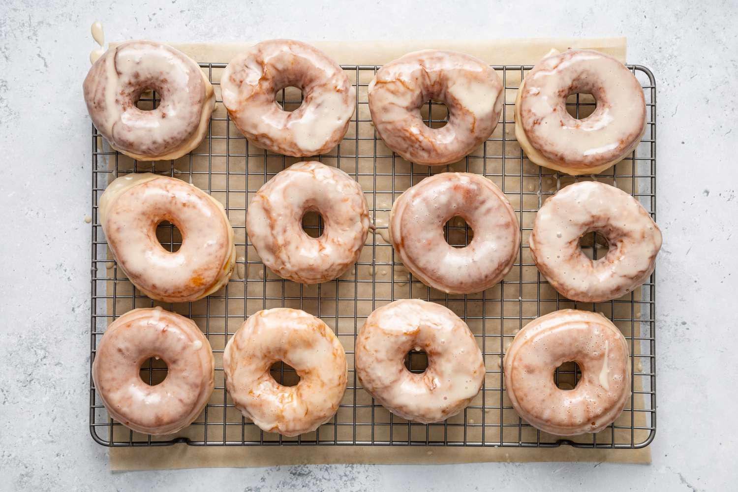 Glazed Donuts Resting on a Wire Rack with Parchment Paper under It 