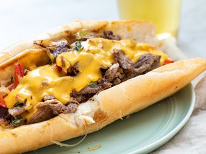 Homemade Philly Cheesesteak on a plate with a tall beer behind it.