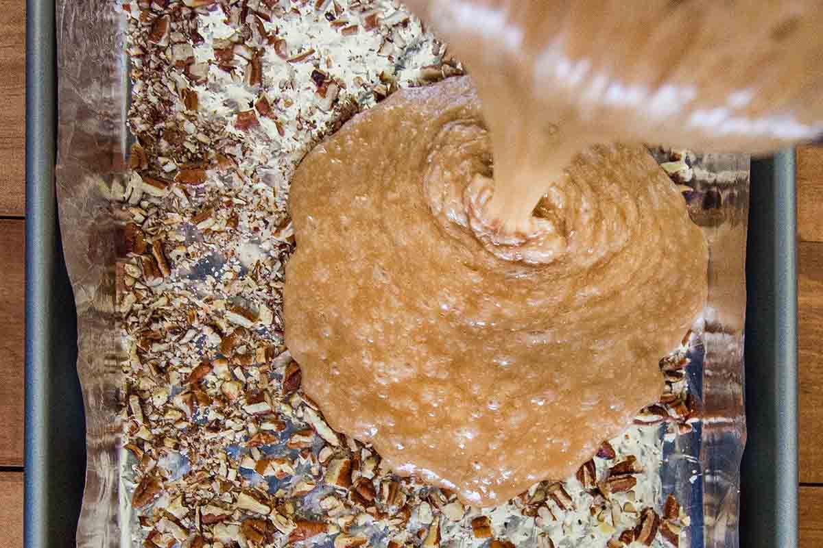 Caramel being poured over top of the nuts to make English toffee.