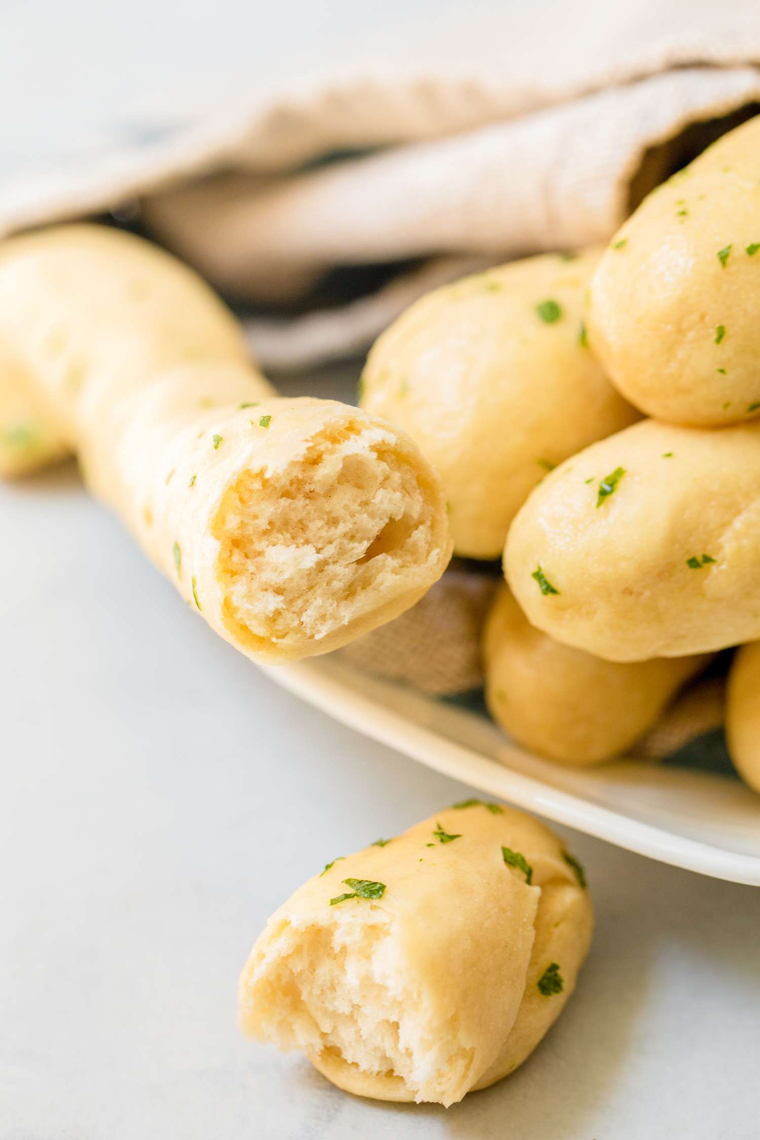 Breadsticks with Garlic Butter on a Plate Covered with a Kitchen Towel (One Breadstick Cut in Half)