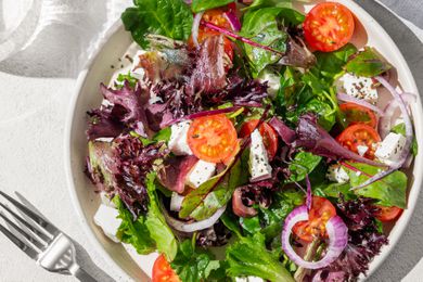 Plate of fresh vegetable salad with mixed greens, cherry tomatoes, feta cheese, and sliced red onions