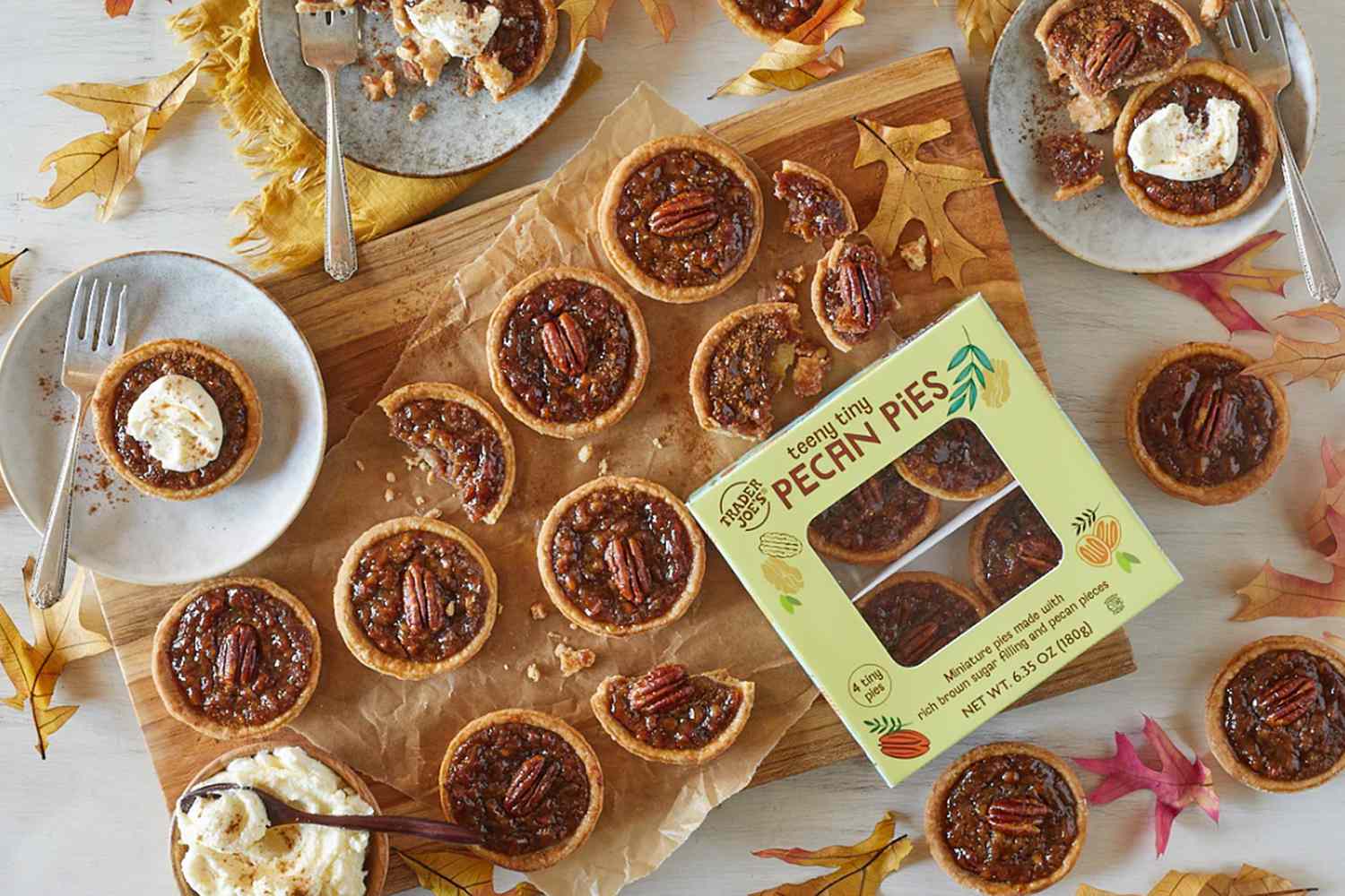 Overhead view of a box of Trader Joe's Teeny Tiny Pecan Pies along with multiple pies on plates and a cutting board