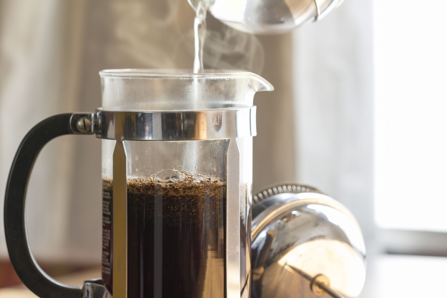 Action shot of hot water being poured into a French press with coffee grounds
