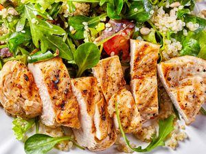 Sliced grilled chicken breast on a bed of greens and quinoa salad