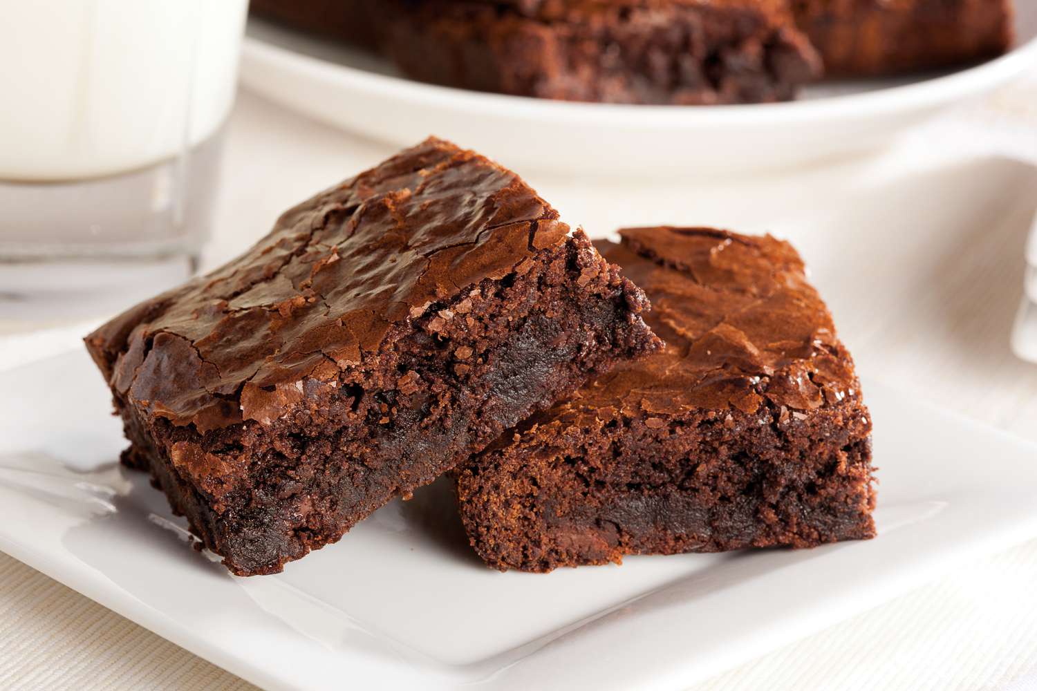 brownies on a plate with a glass of milk and a plate with more brownies in the background