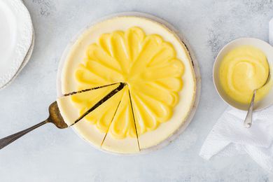 Lemon Cheesecake - whole cheesecake with lemon curd on top and someone is about to take a slice out of it